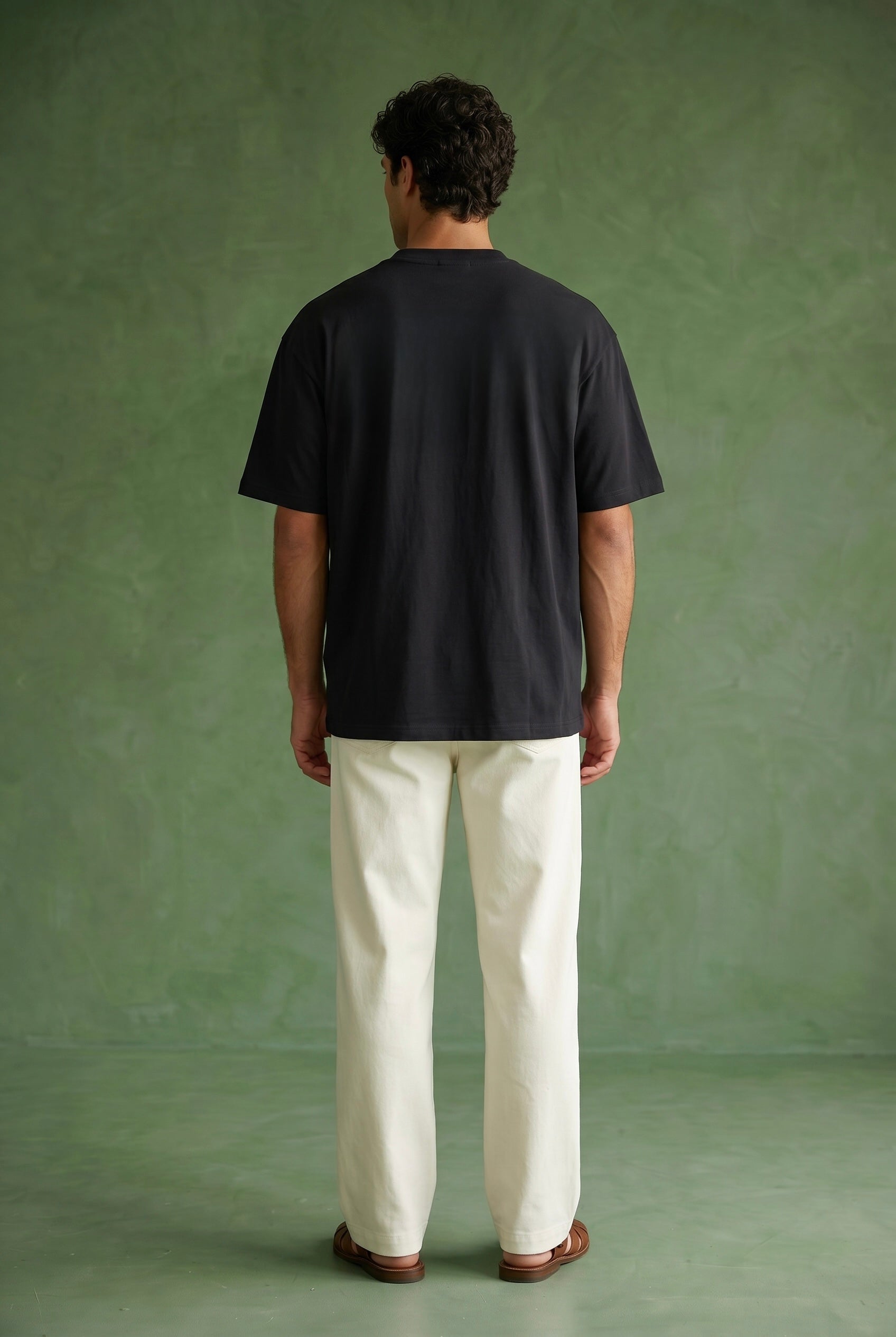 Person wearing a black t-shirt and white pants standing against a green background