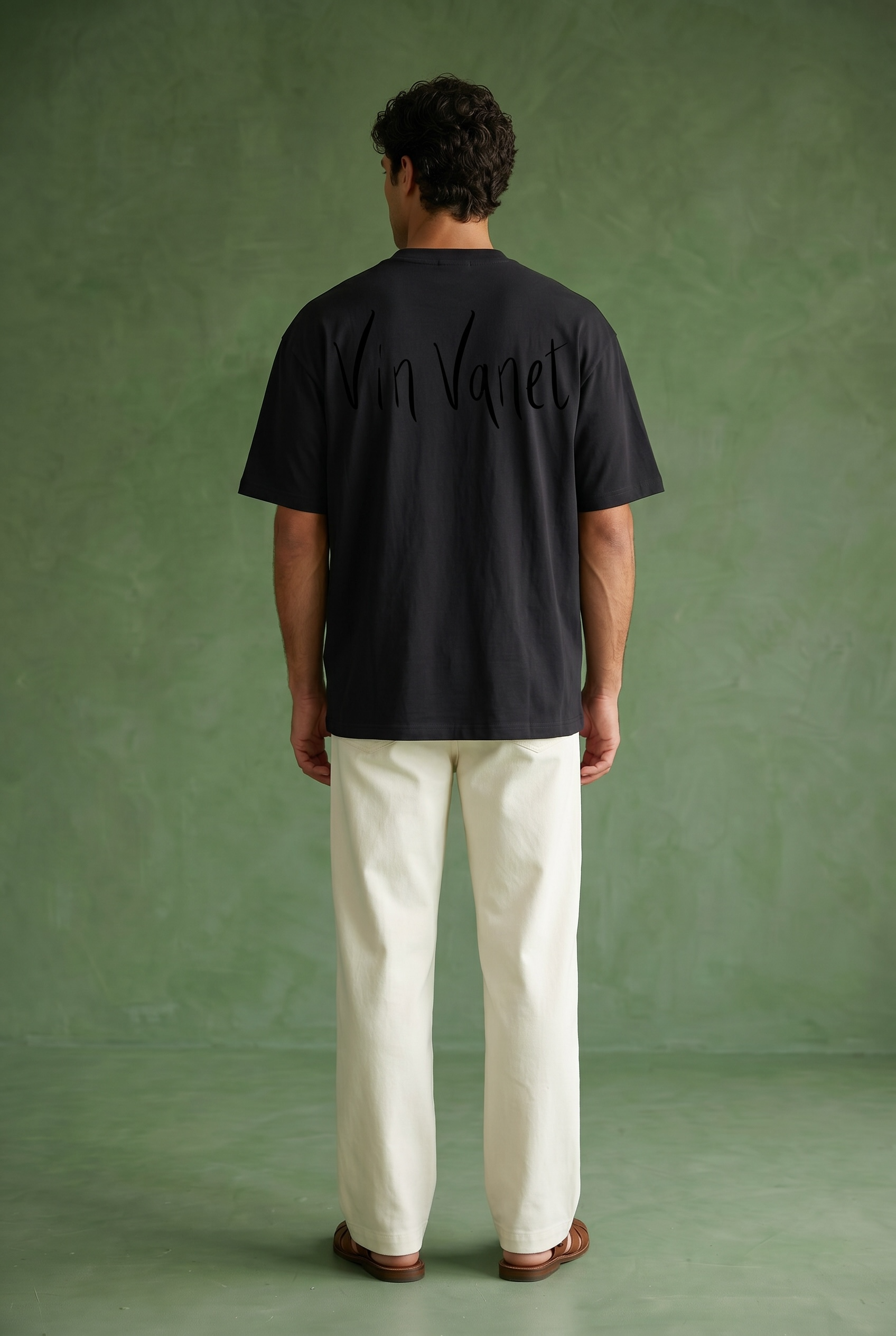 Person wearing a black t-shirt with text on the back vin vanet against a green background