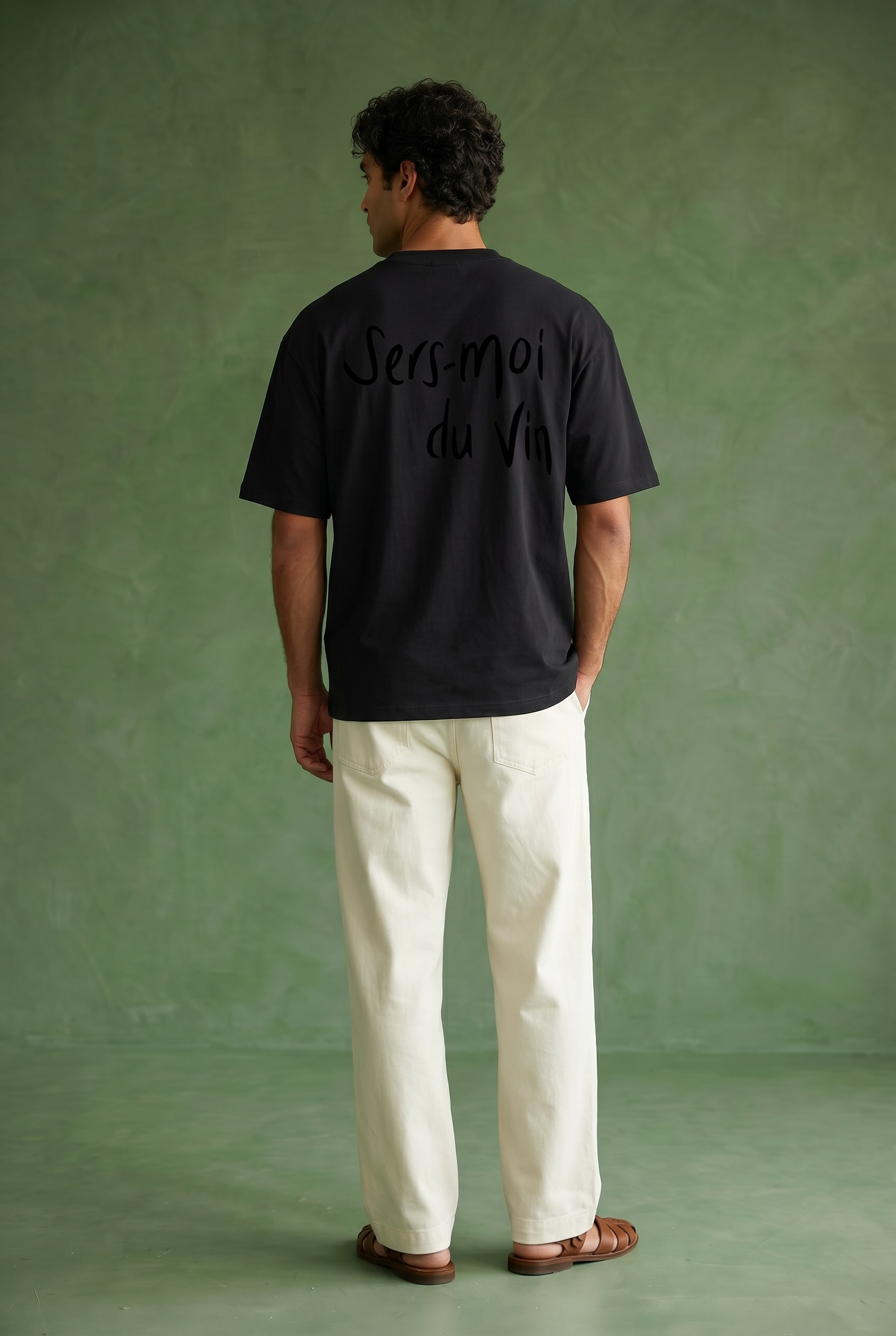 Person wearing a black t-shirt with text on the back that says sers moi du vin against a green background
