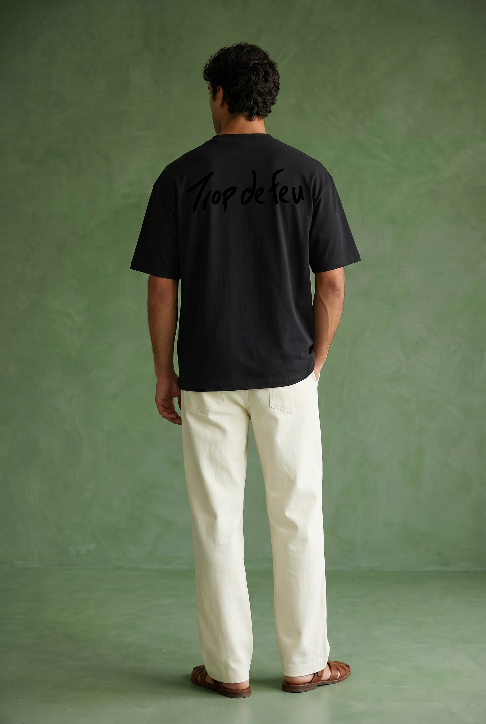 Person wearing a black t-shirt with text on the back that says trop de feu against a green background