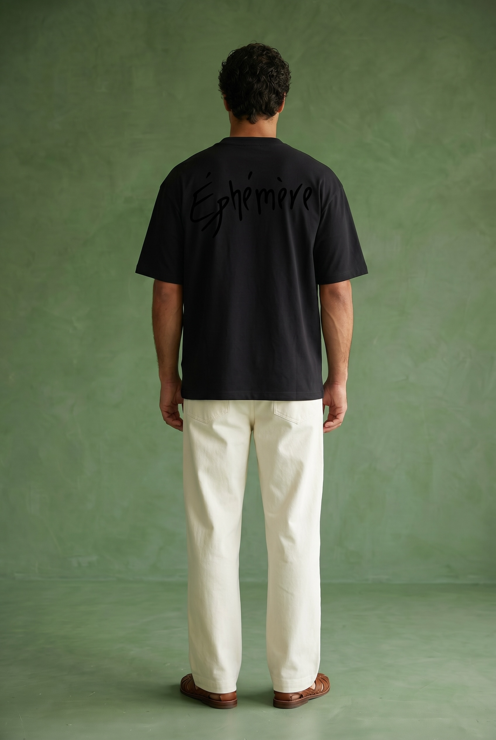 Person wearing a black t-shirt with 'Ephémère' text on the back, standing against a green background.