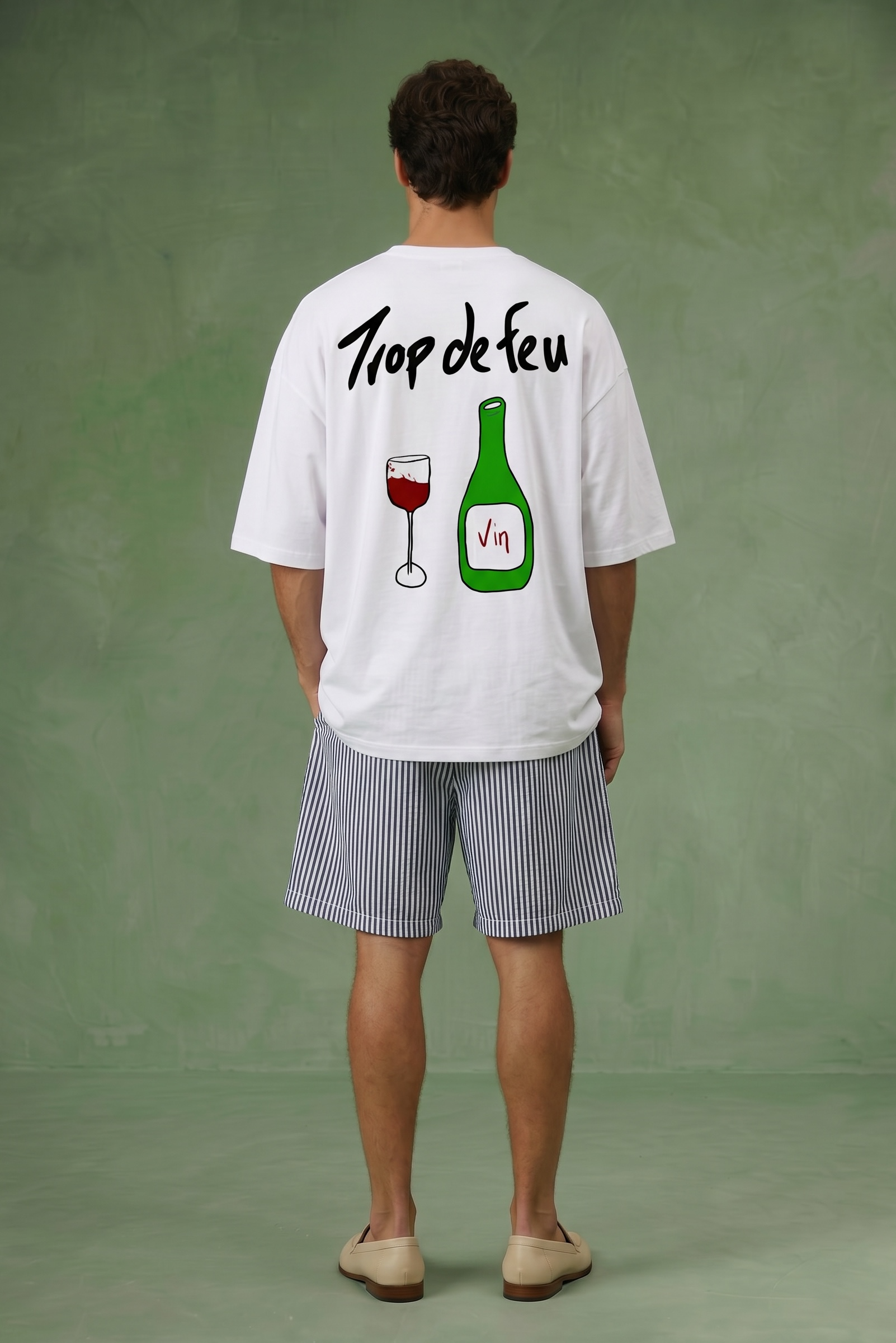 Person wearing a white t-shirt with graphics and text on the back trop de feu, standing against a green background.