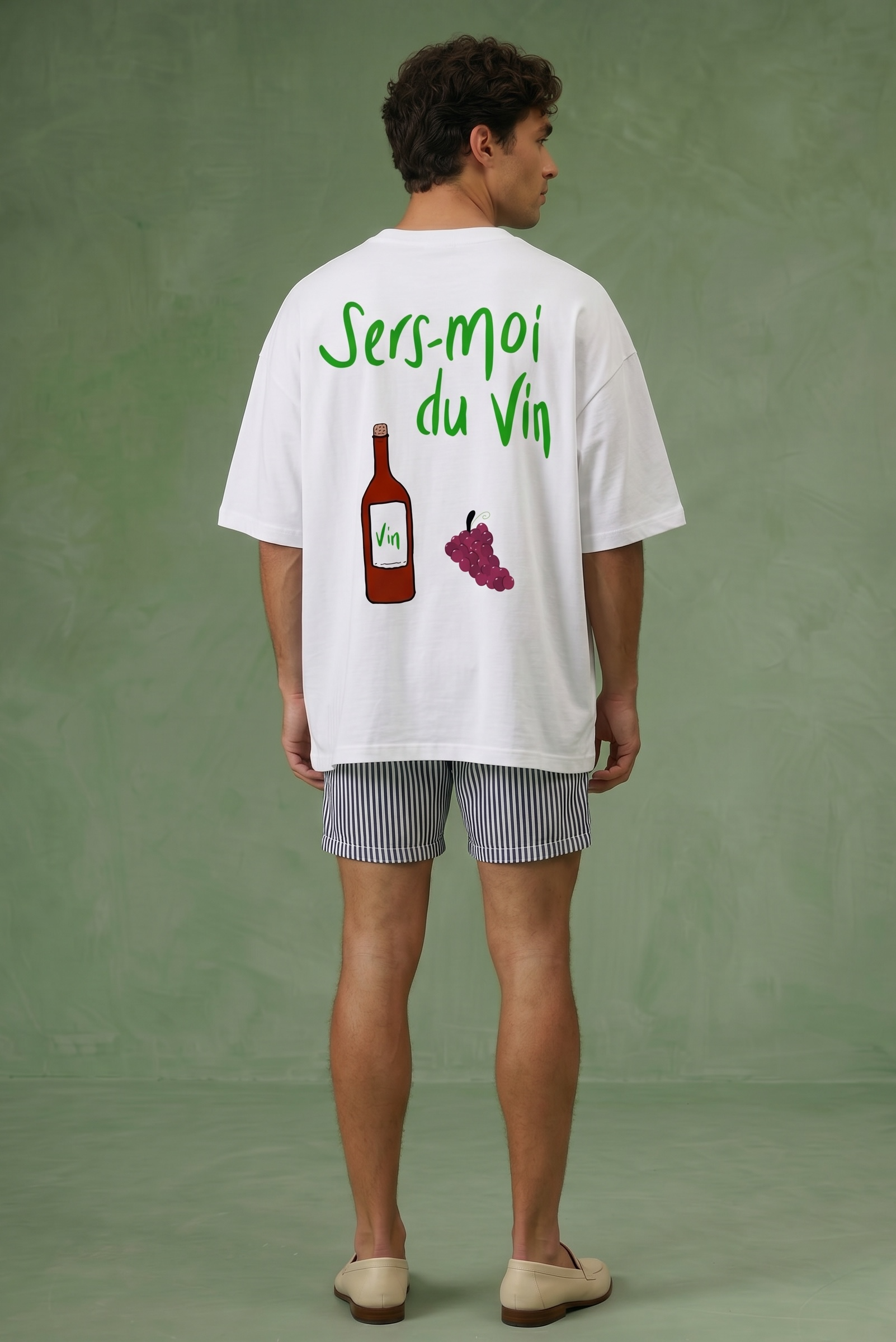 Man wearing a white t-shirt with graphics and text on the back sers moi du vin against a green background
