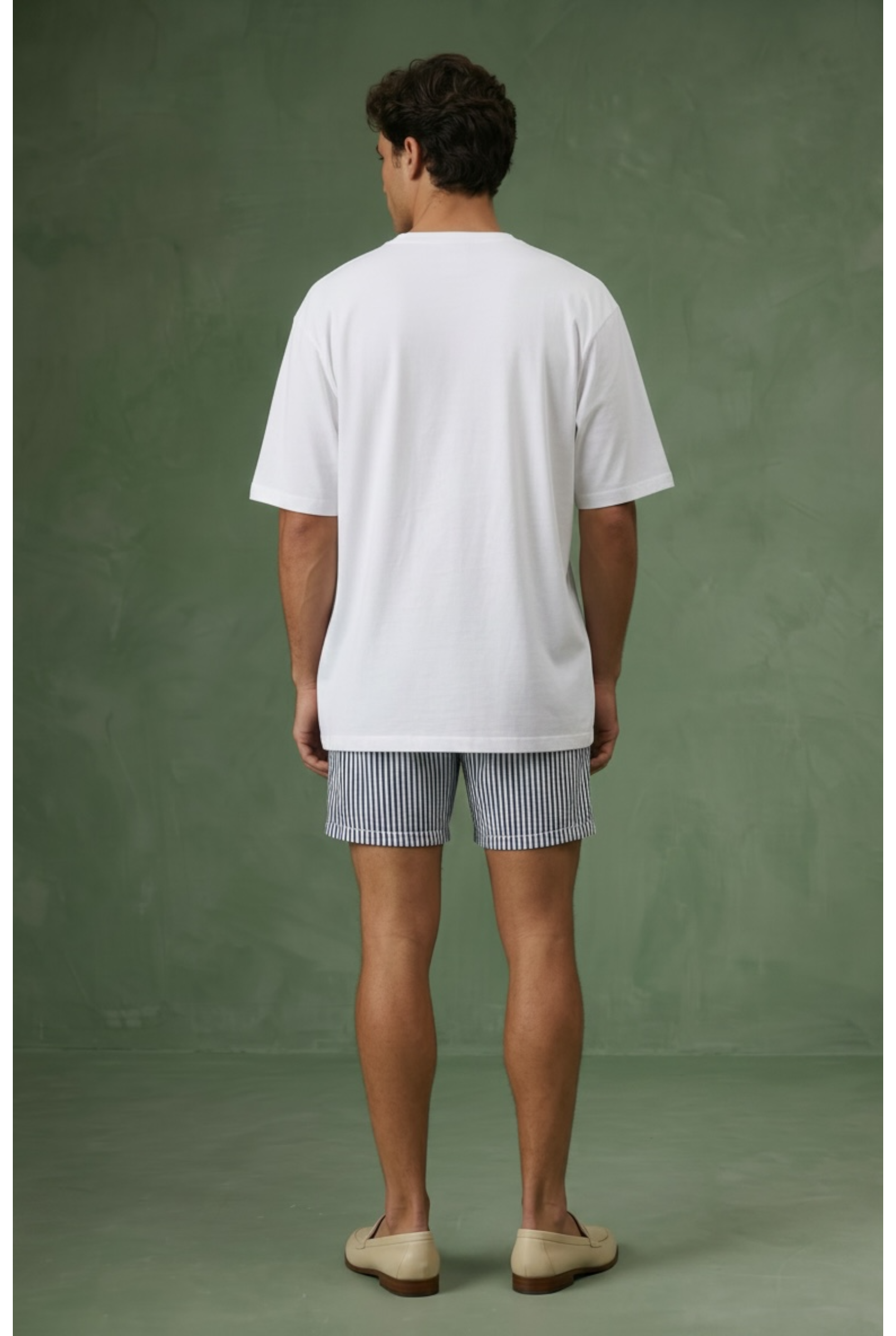 Man wearing a white t-shirt and striped shorts against a green background