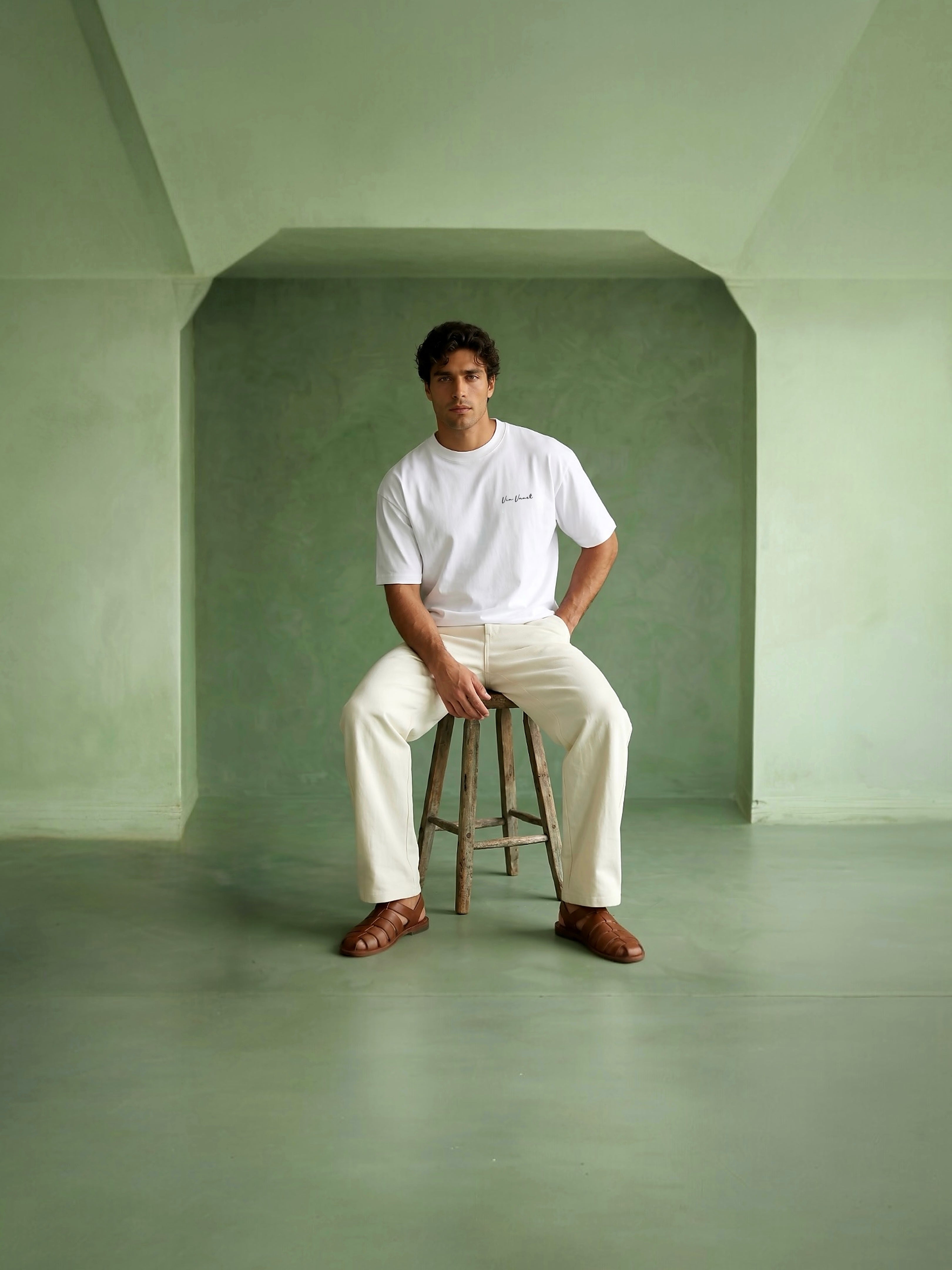 Man sitting on a stool in a minimalistic room with green walls and floor.